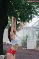 A woman in a white top and red shorts standing under a tree.