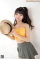 A woman in a yellow top and green skirt holding a straw hat.