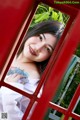 A woman with a tattoo on her arm leaning against a red telephone booth.