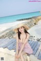 A woman in a pink dress and straw hat sitting on a wooden bench.