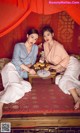 Two women sitting on a bed with a tray of food.