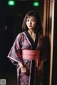 A woman in a pink and black kimono leaning against a wall.