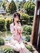 A woman in a pink kimono sitting on the ground next to a pond.