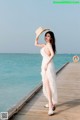 A woman in a white dress and straw hat standing on a pier.