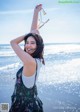 A woman standing on a beach holding a pair of sunglasses.