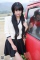 A woman standing next to a red car with her reflection in the window.