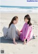 A couple of women sitting on top of a sandy beach.