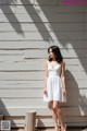 A woman in a white dress standing in front of a white wall.